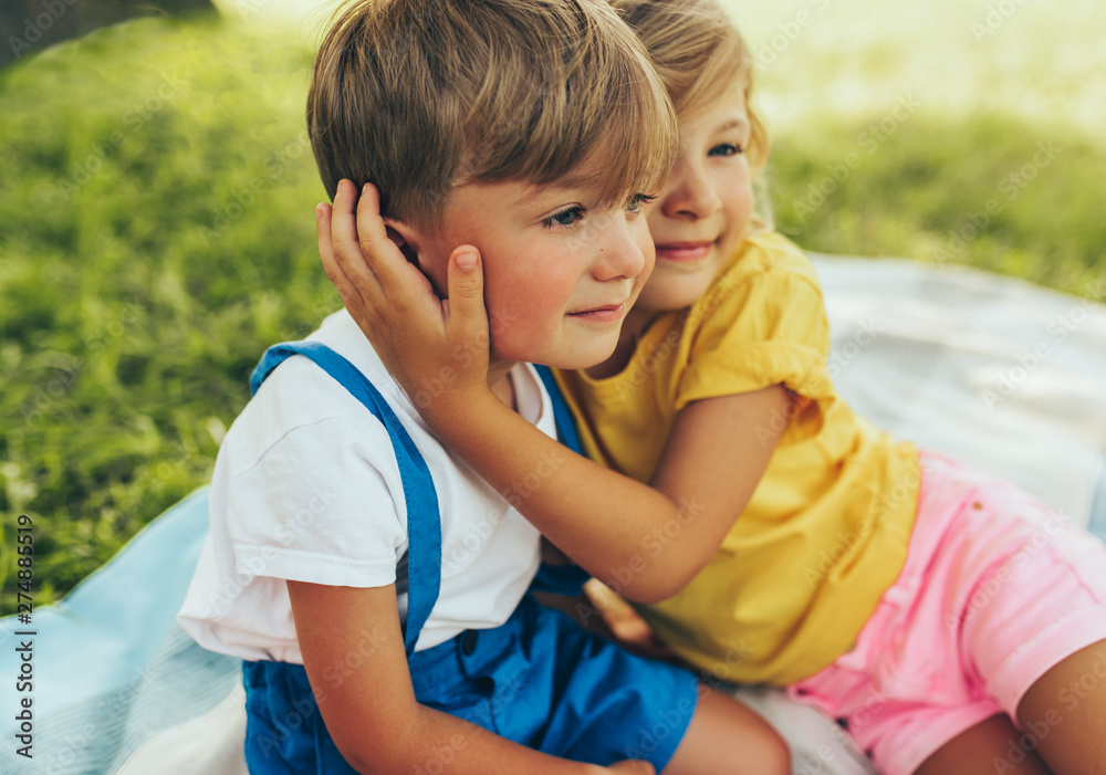 Candid image of smiling two children playing and enjoying the sumemrtime on the blanket outdoors. Sister hugging her little brother in the park. Kids having fun on sunlight. Candid image of smiling two children playing and enjoying the sumemrtime on the blanket outdoors. Sister hugging her little brother in the park. Kids having fun on sunlight.