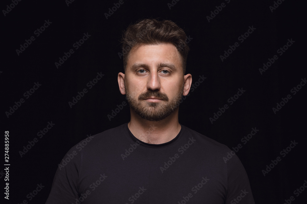 Close up portrait of young caucasian man isolated on black studio background. Photoshot of real emotions of male model. Standing and looks serious. Facial expression, human nature and emotions concept