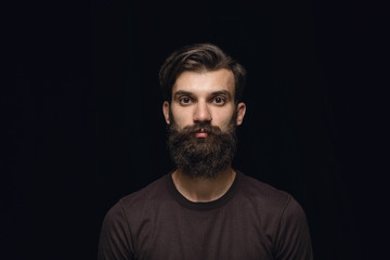 Close up portrait of young caucasian man isolated on black studio background. Photoshot of real emotions of male model. Standing and looks serious. Facial expression, human nature and emotions concept