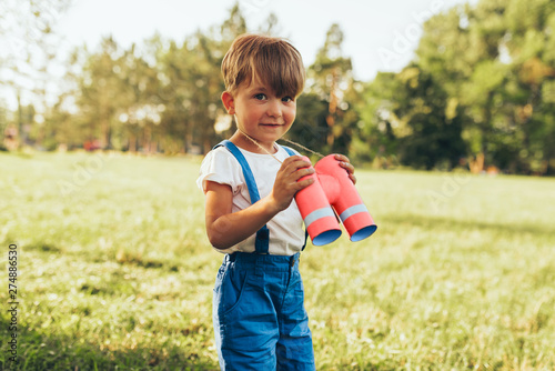 Little boy playing with a binoculars searching for an imagination or exploration in summer day in park. Happy child playing pretend safari game outdoors in the forest. Childhood concept