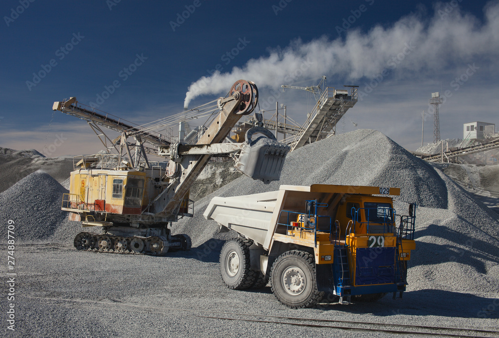 Heavy truck, excavator and rock stone crushing plant against the blue sky in sunny weather. Mining industry. Quarry mining equipment. Heavy truck, excavator and rock stone crushing plant against the blue sky in sunny weather. Mining industry. Quarry mining equipment.