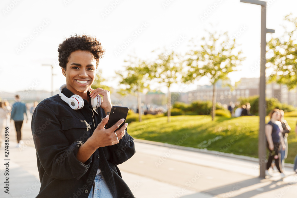 Portrait closeup of smiling african american woman using cellphone and smiling while walking on city street Portrait closeup of smiling african american woman using cellphone and smiling while walking on city street