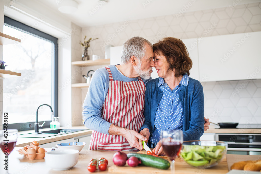 A portrait of senior couple in love indoors at home, cooking. A portrait of senior couple in love indoors at home, cooking.