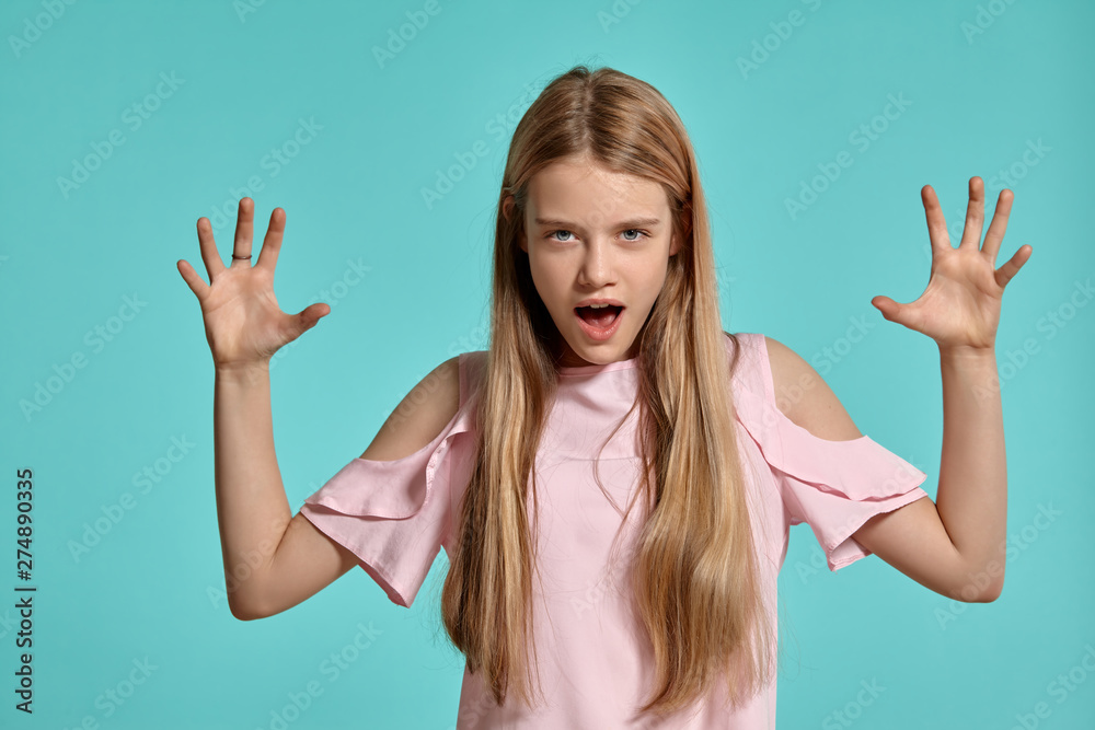 Studio portrait of a beautiful girl blonde teenager in a pink t-shirt posing over a blue background. Studio portrait of a beautiful girl blonde teenager in a pink t-shirt posing over a blue background.