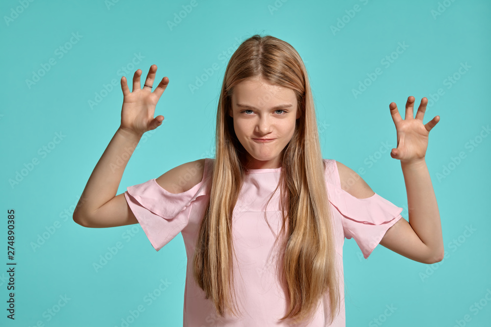 Studio portrait of a beautiful girl blonde teenager in a pink t-shirt posing over a blue background.