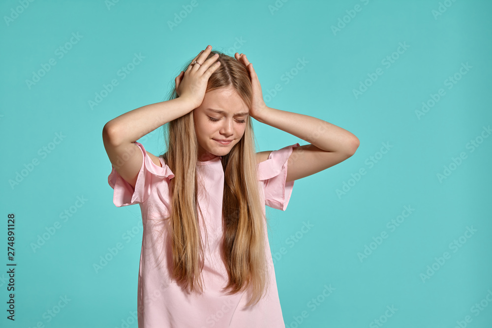 Fototapeta premium Studio portrait of a beautiful girl blonde teenager in a pink t-shirt posing over a blue background.