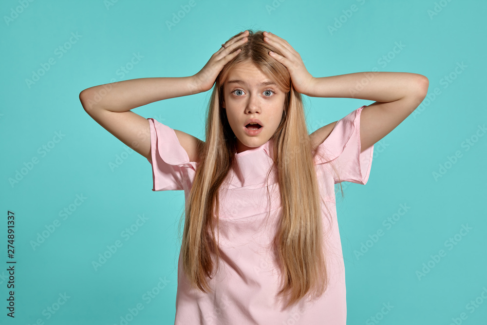 Studio portrait of a beautiful girl blonde teenager in a pink t-shirt posing over a blue background.