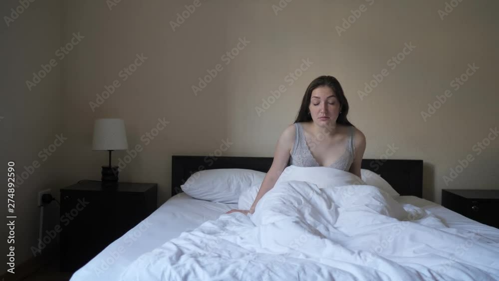 Frightened young woman is waking up, suddenly terrified with nightmare, worries and stress in the middle of the night. She is sitting on bed and falling asleep. Nightmares and insomnia. Frightened young woman is waking up, suddenly terrified with nightmare, worries and stress in the middle of the night. She is sitting on bed and falling asleep. Nightmares and insomnia.