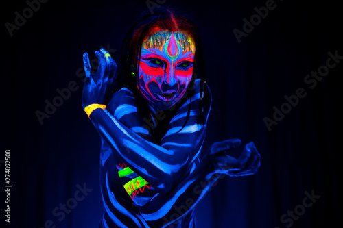 Close-up Portrait of Wild and frantic Young naked bodyarted woman in blue glowing ultraviolet paint and Yellow eye lenses. Avatar entity amazon warrior girl with pigtails hairstyle