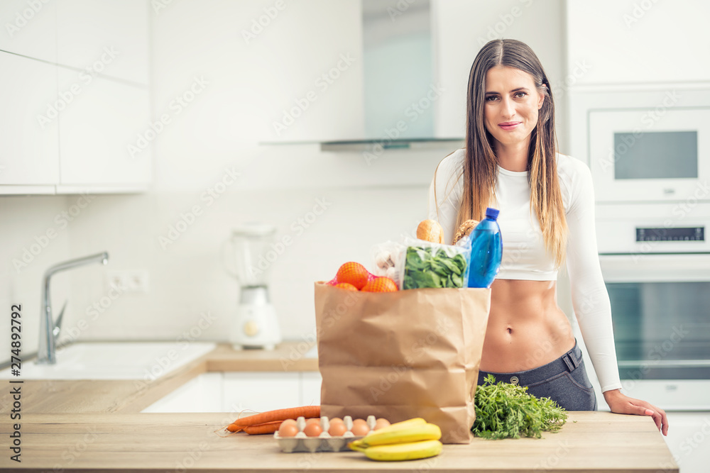 Young woman standing in kitchen with purchase on table