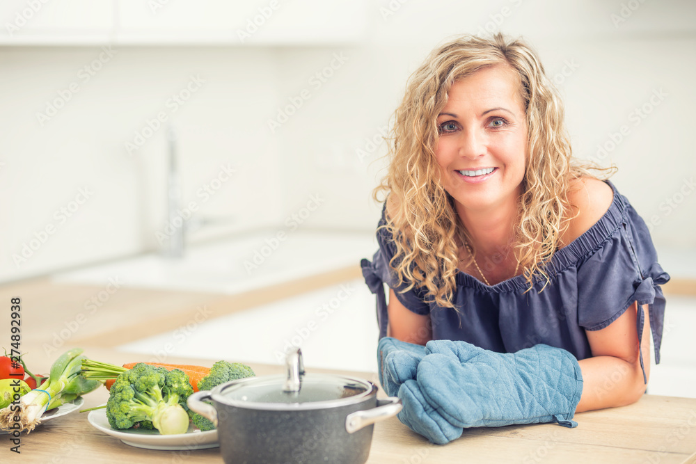 Portrait of happy adult woman in her modern kitchen with pot and vegetables Portrait of happy adult woman in her modern kitchen with pot and vegetables