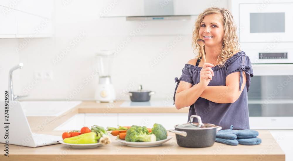 Portrait of happy adult woman in her modern kitchen with pot and vegetables Portrait of happy adult woman in her modern kitchen with pot and vegetables
