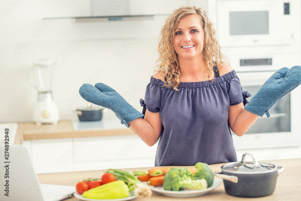 Portrait of happy adult woman in her modern kitchen with pot and vegetables