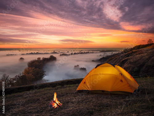 Orange lit inside tent and fire over misty river at sunset photo
