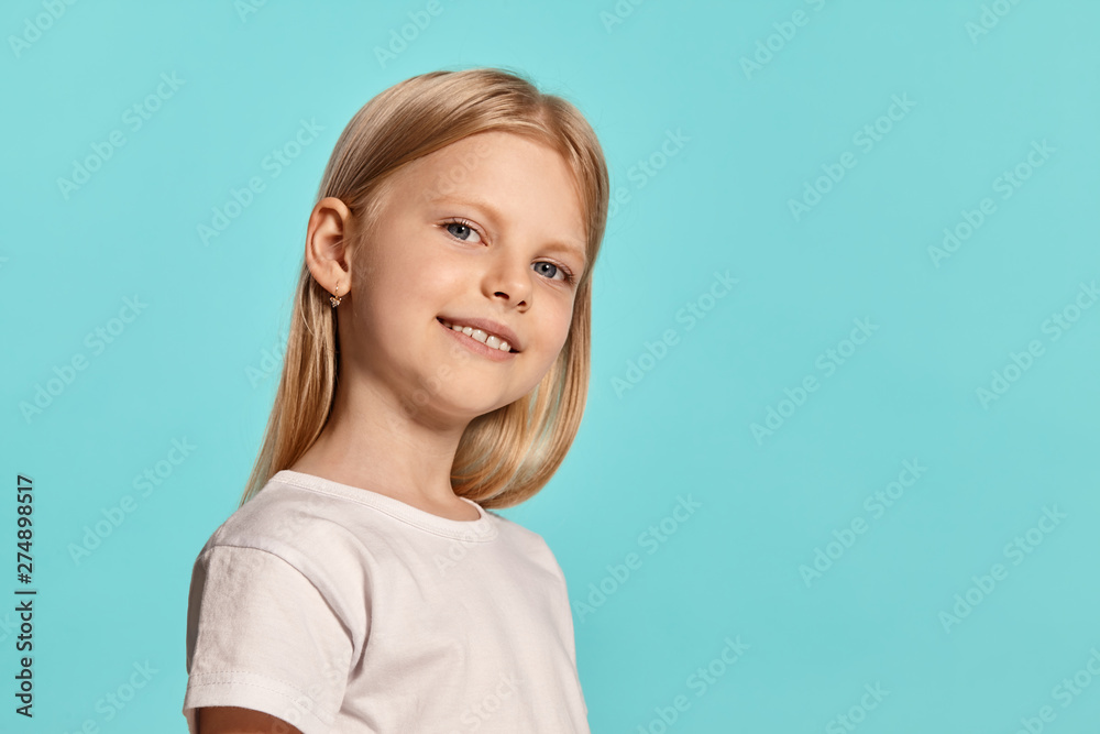 Close-up studio shot of a lovely blonde little girl in a white t-shirt posing against a blue background. Close-up studio shot of a lovely blonde little girl in a white t-shirt posing against a blue background.