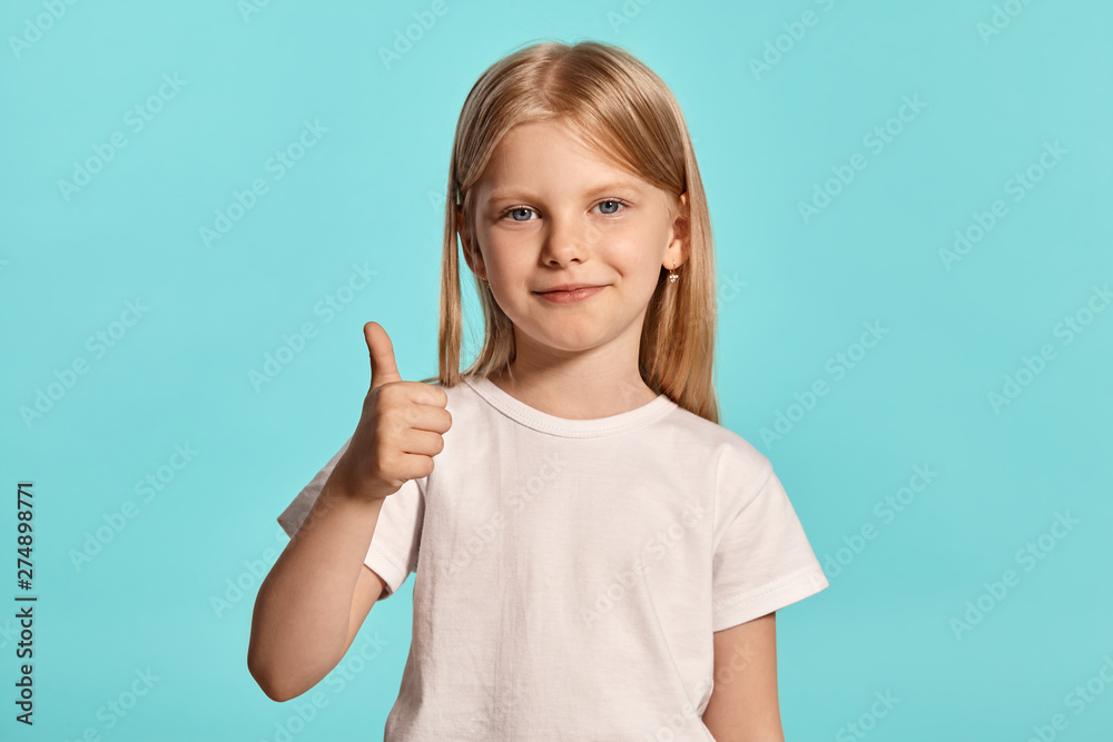 Close-up studio shot of a lovely blonde little girl in a white t-shirt posing against a blue background. Close-up studio shot of a lovely blonde little girl in a white t-shirt posing against a blue background.