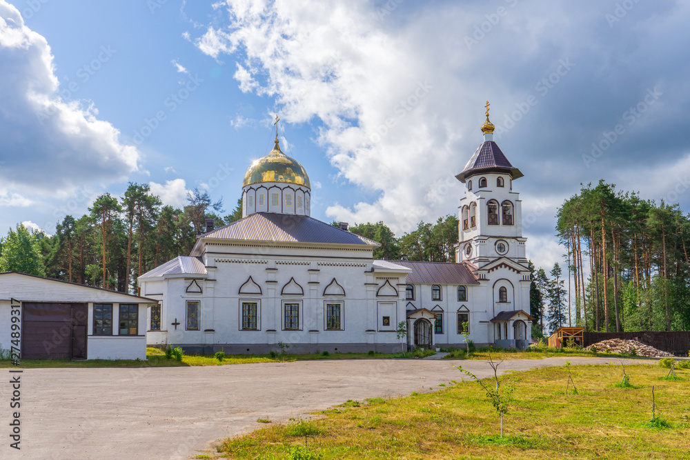 Church to St. Grand Prince Alexander Nevsky in Pudozh after restoration. Orthodox temple and bell tower against northern pine forest and blue sky in summer sunny day. Karelia, Russia