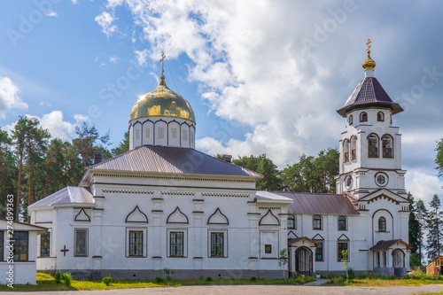 Church to St. Grand Prince Alexander Nevsky in Pudozh after restoration. Orthodox temple and bell tower against northern pine forest and blue sky in summer sunny day. Karelia, Russia