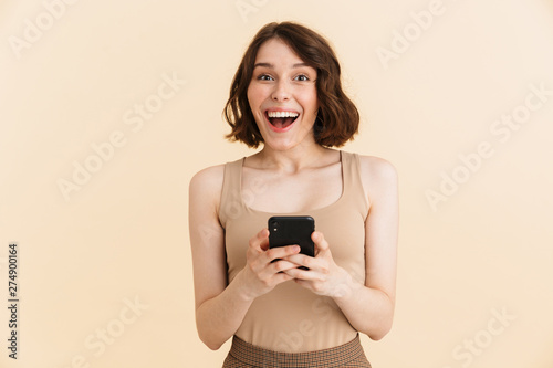 Portrait of amazed caucasian woman 20s dressed in casual clothes smiling while holding cellphone