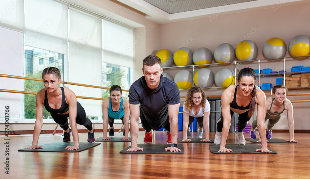 A group of sporting young people in sportswear, in a fitness room, doing push-ups or planks in the gym. Group fitness concept, group workouts, motivation