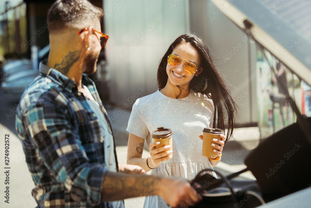 Young couple preparing for vacation trip on the car in sunny day. Woman and man drinking coffee and ready for going to sea or ocean. Concept of relationship, vacation, summer, holiday, weekend.