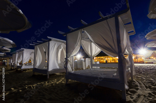 White beach bed with white tent curtains at night. Luxury beach tents at beach resort near restaurant. Summer beach vacation and relaxation concept