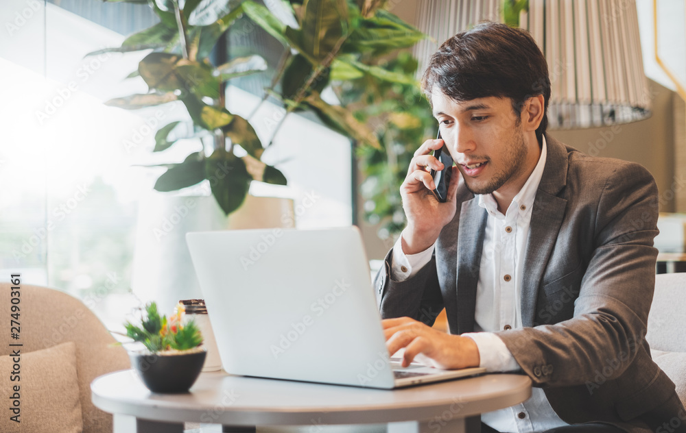 Asian businessman using laptop and mobile phone while working in office Asian businessman using laptop and mobile phone while working in office