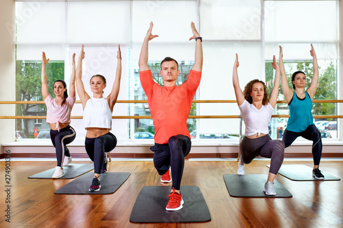 Group of young sporty attractive people practicing yoga lesson with instructor  standing together in exercise  working out  full length  studio background  close up
