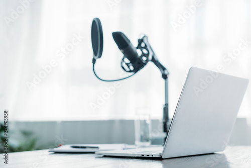 selective focus of laptop near microphone on desk in broadcasting studio