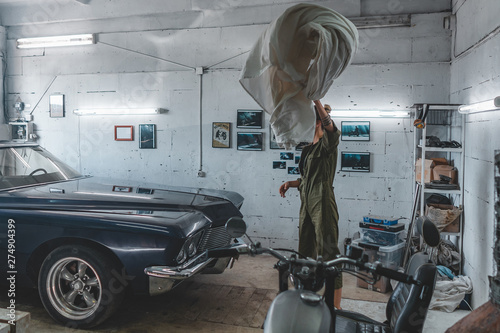 Attractive Caucasian female removing cover from her vintage old car in a garage