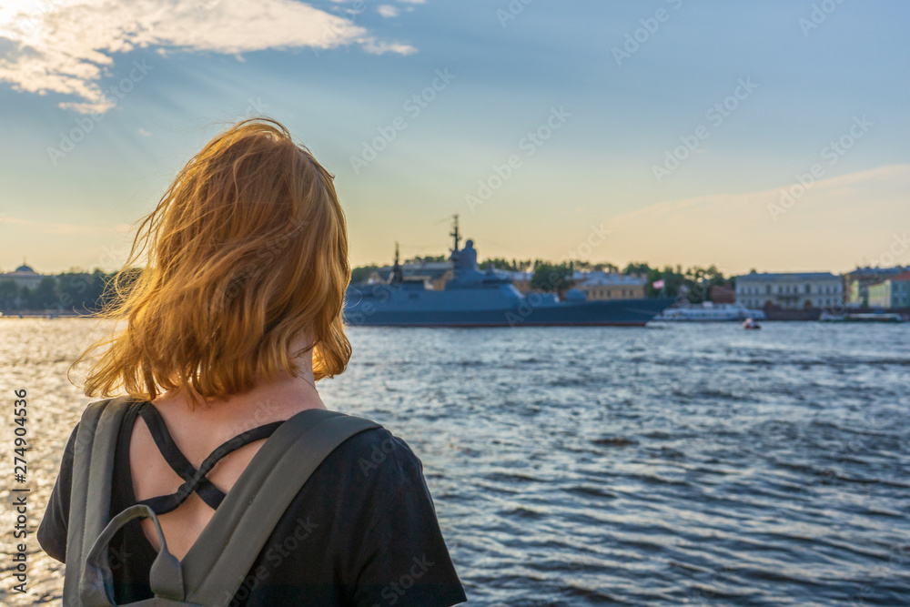 Redhead tween tourist girl on Neva river embankment looking at warships and architectural ensemble in summer evening at sunset. Authentic lifestyle moments, travel concept. Saint Petersburg, Russia Redhead tween tourist girl on Neva river embankment looking at warships and architectural ensemble in summer evening at sunset. Authentic lifestyle moments, travel concept. Saint Petersburg, Russia