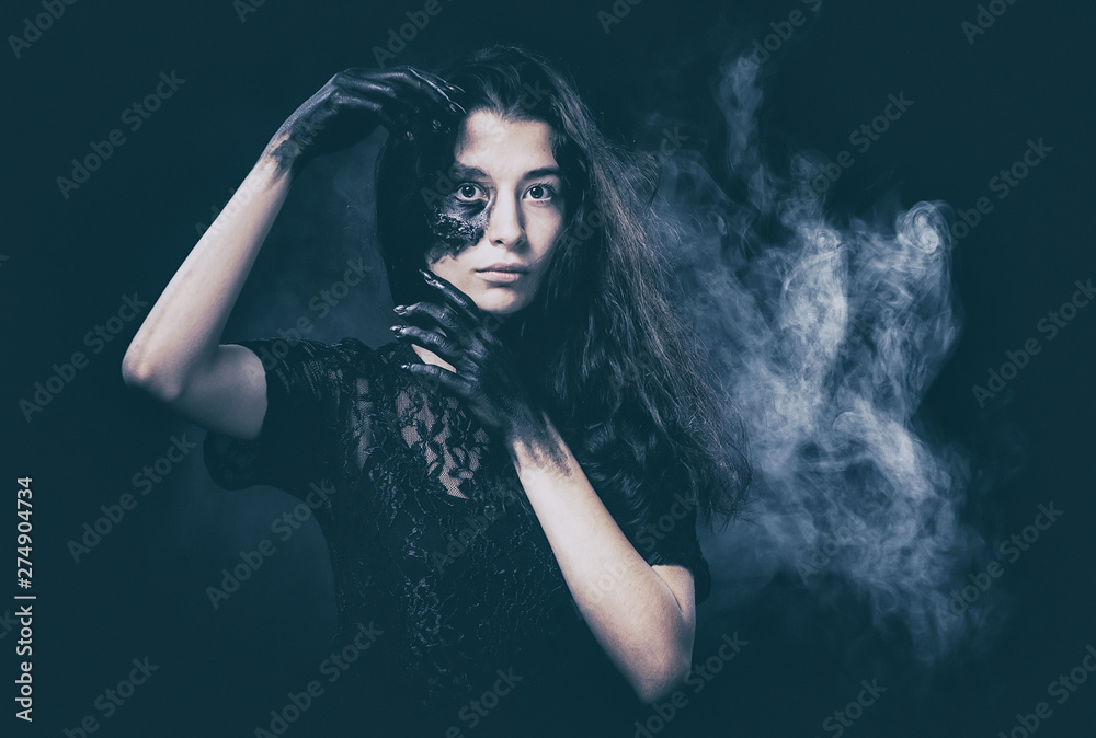 a young succubus girl on a smoke background with hands stained with soot and a burned face with an expressive look and a pleasant appearance in a black dress