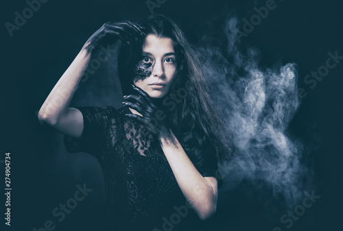 a young succubus girl on a smoke background with hands stained with soot and a burned face with an expressive look and a pleasant appearance in a black dress photo