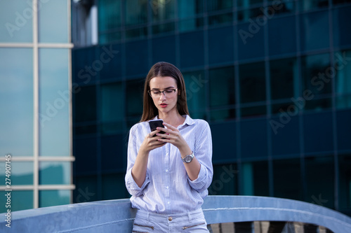 Executive business woman looking at mobile smartphone in the street with office buildings in the background