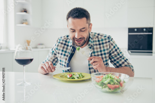 Portrait of charming imposing man hold hand silverware knife fork sit table enjoy meal morning breakfast checkered shirt clothes big light appartment room wineglass