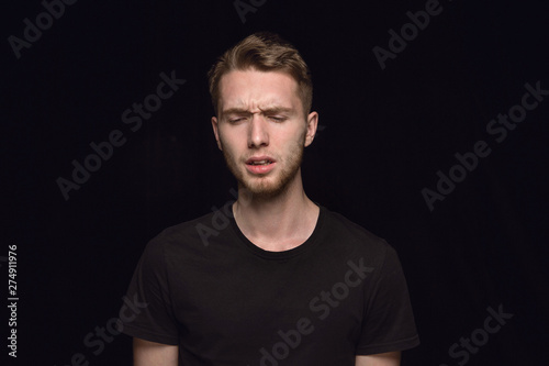 Close up portrait of young caucasian man isolated on black studio background. Photoshot of real emotions of male model. Mourning, mental suffering. Facial expression, human nature and emotions concept