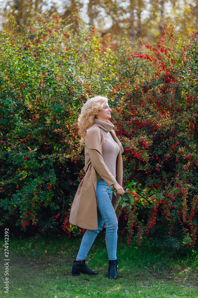Beautiful elegant woman standing next barberry bush in autumn park