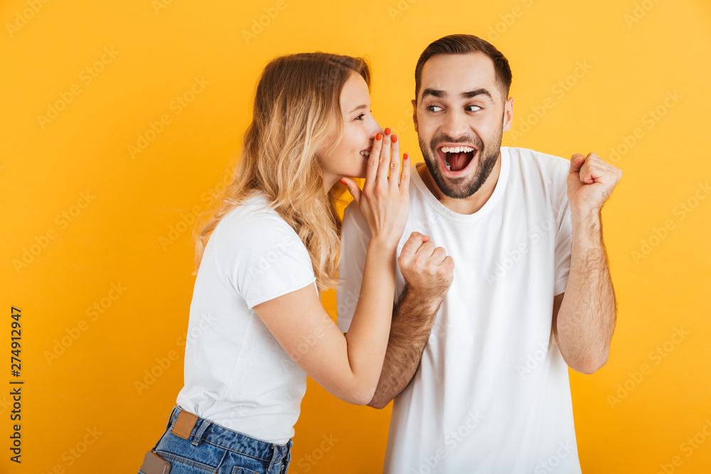 Image of ecstatic couple man and woman in basic t-shirts whispering secrets or gossips to each other Image of ecstatic couple man and woman in basic t-shirts whispering secrets or gossips to each other