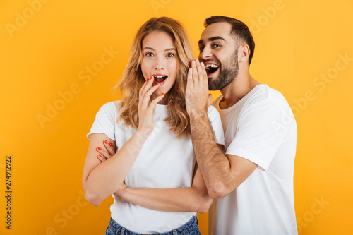 Image of attractive couple man and woman in basic t-shirts whispering secrets or gossips to each other photo