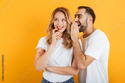 Image of happy couple man and woman in basic t-shirts whispering secrets or gossips to each other photo