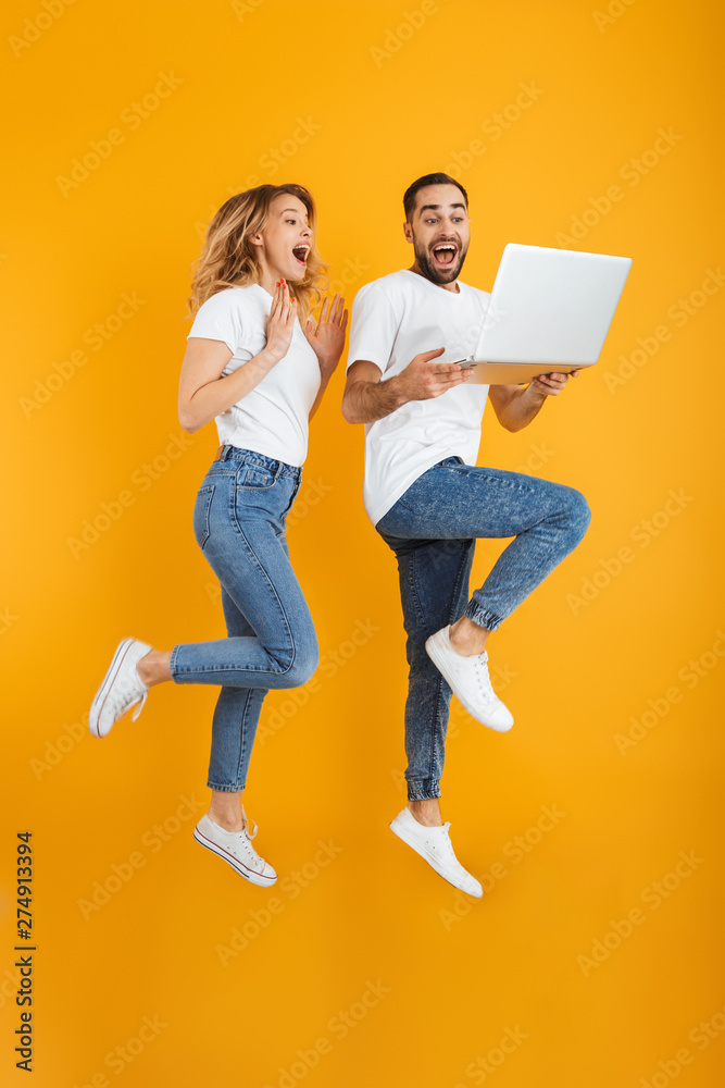Full length image of excited couple man and woman rejoicing while holding laptop together - obrazy, fototapety, plakaty 