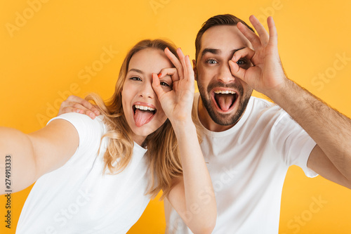 Image of joyful couple rejoicing and sticking out tongues while showing ok sign together