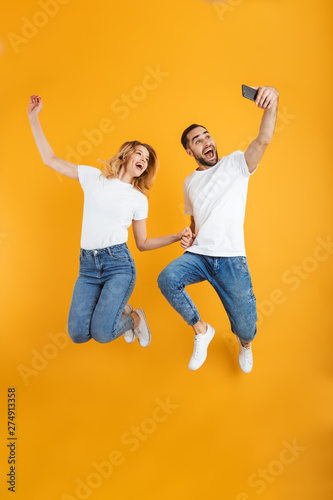 Full length image of cheerful couple rejoicing and jumping while taking selfie photo on cellphone