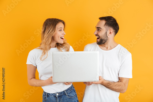 Image of pretty couple man and woman rejoicing while holding laptop together