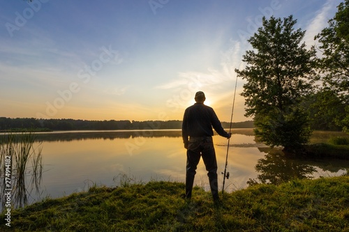 Silhouette of angler standing on the shore of the lake during sunrise