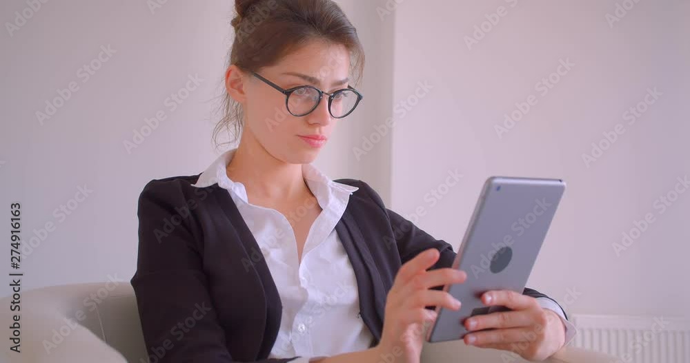 Closeup shoot of young pretty caucasian businesswoman using the tablet sitting in the armchair in the office indoors in a white room Closeup shoot of young pretty caucasian businesswoman using the tablet sitting in the armchair in the office indoors in a white room