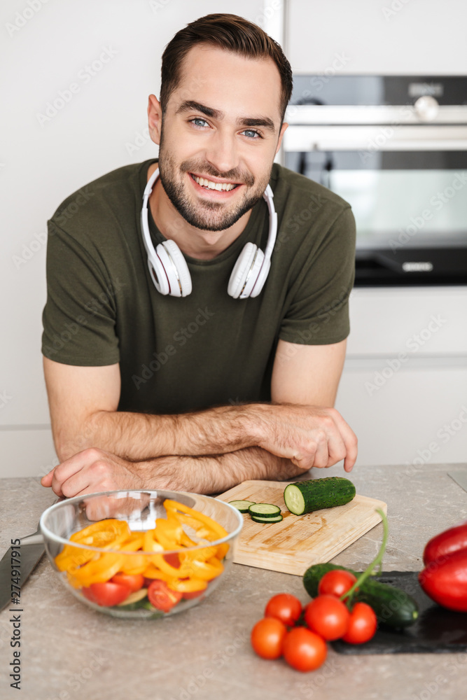 Happy young handsome man posing at the kitchen at home cooking listening music with headphones. Happy young handsome man posing at the kitchen at home cooking listening music with headphones.
