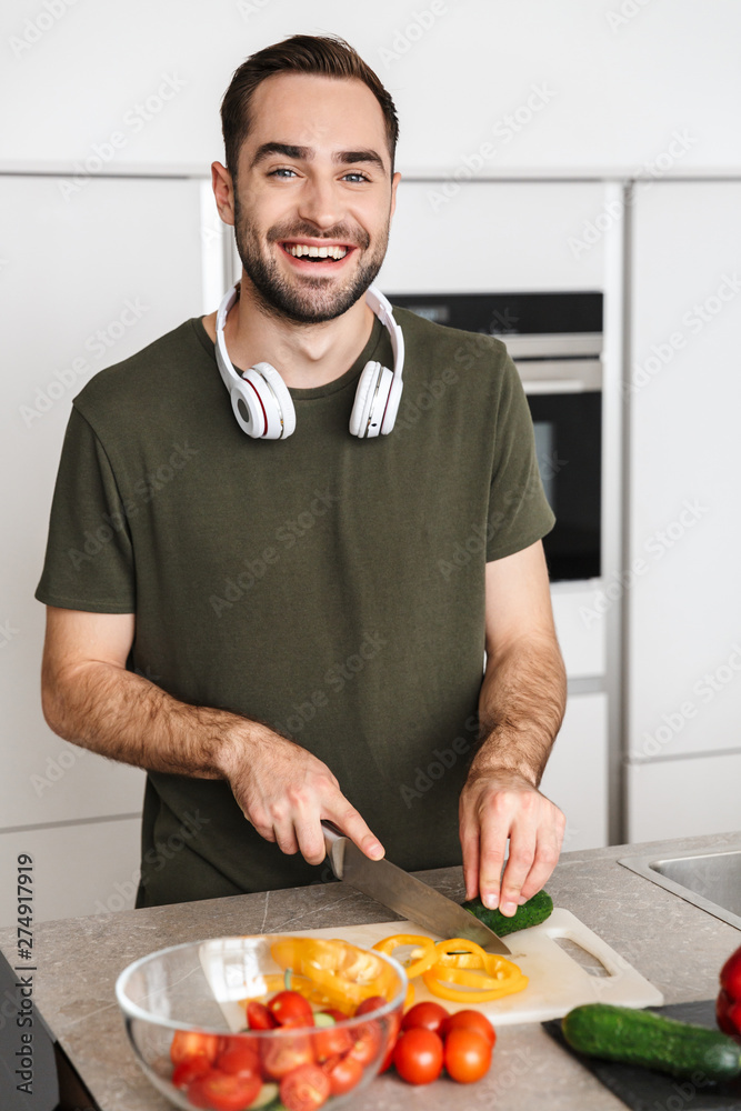 Happy young handsome man posing at the kitchen at home cooking listening music with headphones. Happy young handsome man posing at the kitchen at home cooking listening music with headphones.