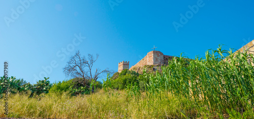 Panorama of the colorful town of Bosa along a river and hills in sunlight in spring