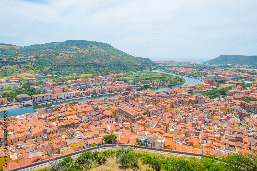 Panorama of the colorful town of Bosa along a river and hills in sunlight in spring